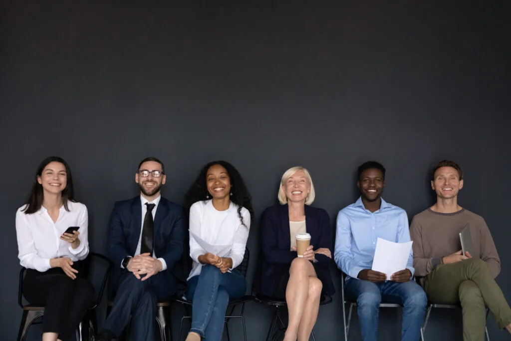 Near black wall studio background sitting six diverse happy entrepreneurs, successful corporate staff members, businesspeople ready for negotiation, wait for job interview sit in row queue, hr concept