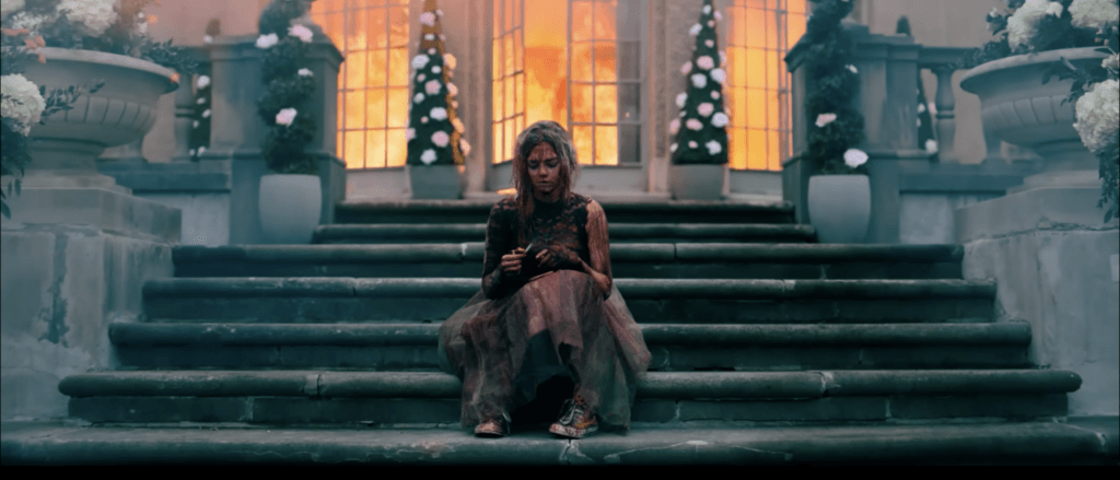 Samara Weaving, as Grace, sitting on steps outside burning building at beginning of Ready or Not 2 Here I Come Movie
