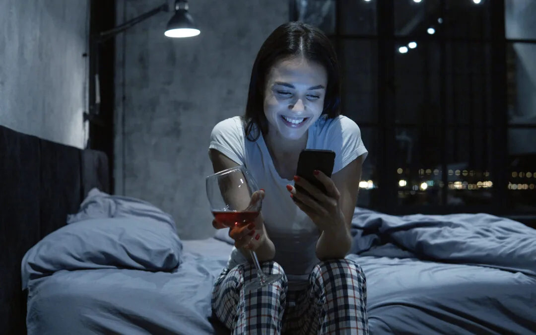 STD Test Results on phone young woman looking at smartphone, using online dating app, drinking wine, sitting on bed at night