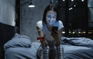 STD Test Results on phone young woman looking at smartphone, using online dating app, drinking wine, sitting on bed at night